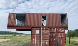 Dom z kontenerów w budowie, kobieta stoi w drzwiach górnego kontenera.