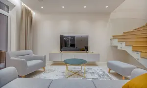 Nowoczesny salon z szarymi meblami, telewizorem i drewnianymi schodami. Minimalizm w domu podkreśla harmonię i spokój.