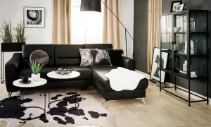 Nowoczesny salon z czarną ścianą w tle. Czarna skórzana kanapa, białe stoliki kawowe, dywan w cętki i szklana witryna tworzą elegancką przestrzeń.