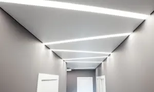 Nowoczesny korytarz z geometrycznymi wzorami sufitu napinanego i wbudowanym oświetleniem LED.