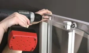 Montaż kabiny prysznicowej szklanej: wkręcanie śruby w profil aluminiowy za pomocą wiertarko-wkrętarki.