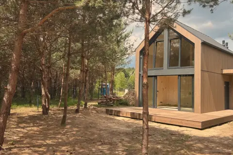 Nowoczesny dom jednorodzinny z drewnianą elewacją i dużymi oknami, otoczony sosnowym lasem.