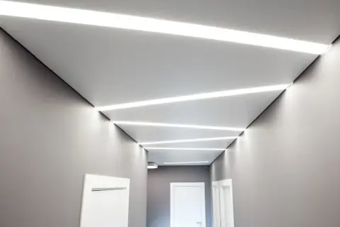 Nowoczesny korytarz z geometrycznymi wzorami sufitu napinanego i wbudowanym oświetleniem LED.