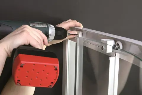 Montaż kabiny prysznicowej szklanej: wkręcanie śruby w profil aluminiowy za pomocą wiertarko-wkrętarki.