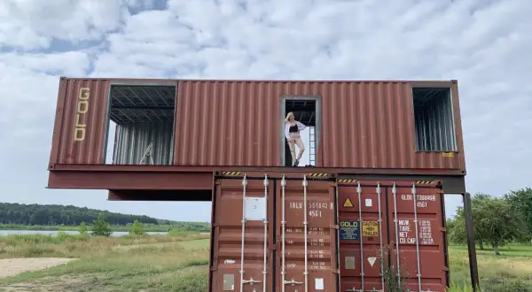 Dom z kontenerów w budowie, kobieta stoi w drzwiach górnego kontenera.