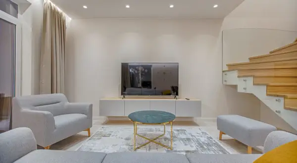Nowoczesny salon z szarymi meblami, telewizorem i drewnianymi schodami. Minimalizm w domu podkreśla harmonię i spokój.