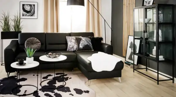 Nowoczesny salon z czarną ścianą w tle. Czarna skórzana kanapa, białe stoliki kawowe, dywan w cętki i szklana witryna tworzą elegancką przestrzeń.