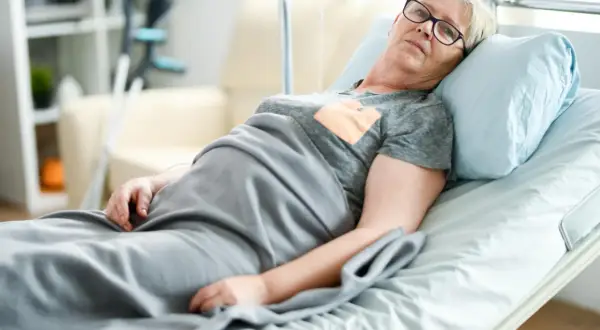 Starsza kobieta w łóżku szpitalnym, oczekująca na zlecenie na materac przeciwodleżynowy.