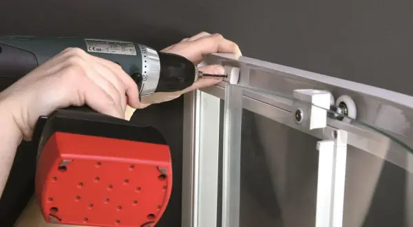 Montaż kabiny prysznicowej szklanej: wkręcanie śruby w profil aluminiowy za pomocą wiertarko-wkrętarki.