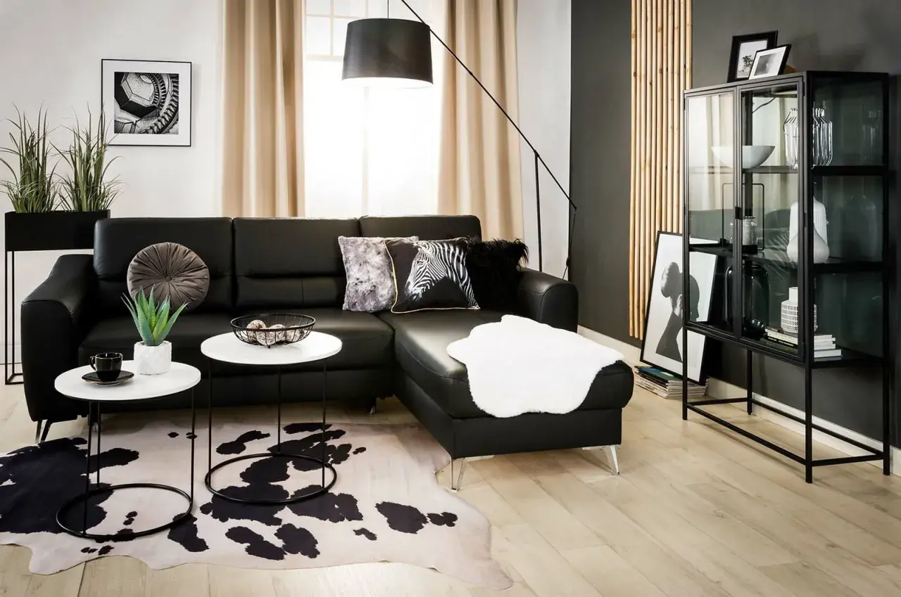 Nowoczesny salon z czarną ścianą w tle. Czarna skórzana kanapa, białe stoliki kawowe, dywan w cętki i szklana witryna tworzą elegancką przestrzeń.