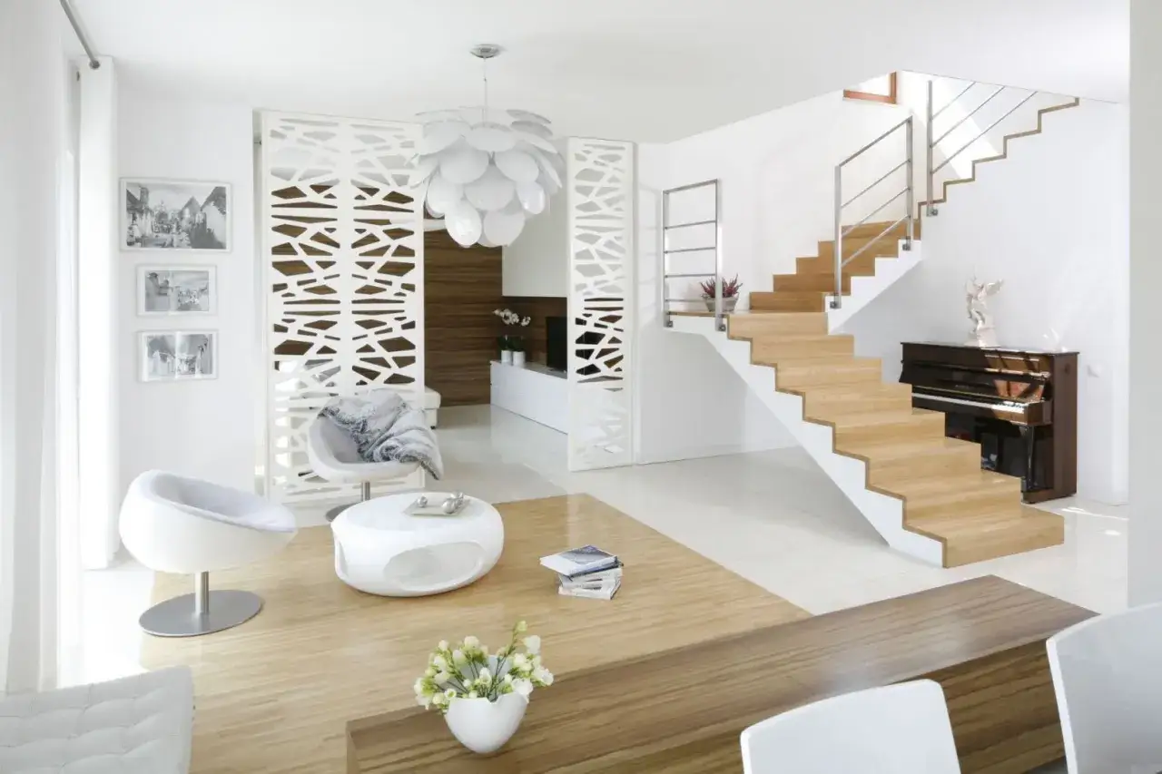 Jasny, przestronny salon w stylu minimalistycznym. Drewniane schody, białe meble, ażurowa ścianka działowa i fortepian tworzą elegancką całość.