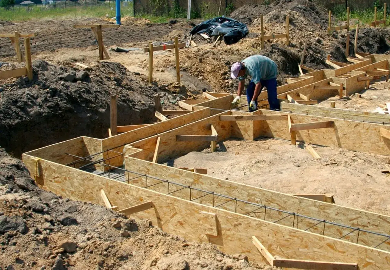 Budowa fundamentów: pracownik montuje szalunek z desek, przygotowując miejsce pod beton.