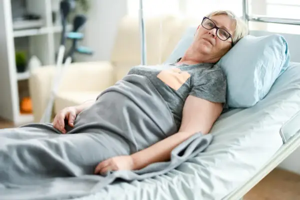 Starsza kobieta w łóżku szpitalnym, oczekująca na zlecenie na materac przeciwodleżynowy.