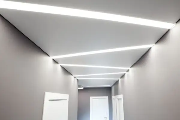Nowoczesny korytarz z geometrycznymi wzorami sufitu napinanego i wbudowanym oświetleniem LED.